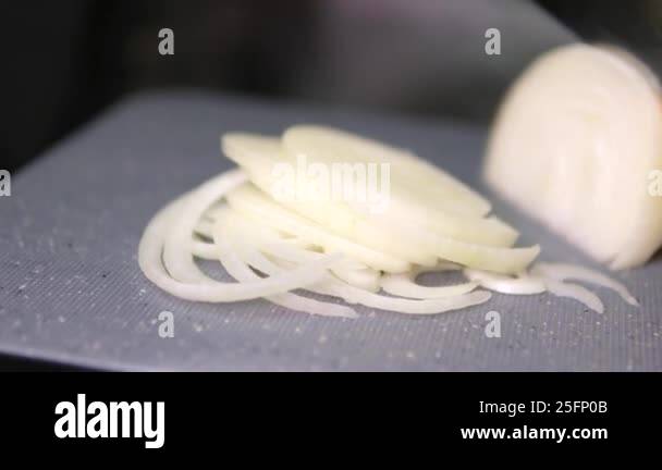 Chopping raw onion with a kitchen knife on a wooden cutting board ...