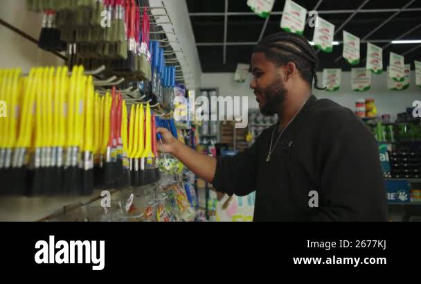 Man arranging tools and brushes on racks in a paint store, holding a ...