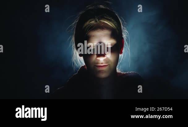 A chilling portrait of a teenage girl in the darkness, lit by dramatic ...