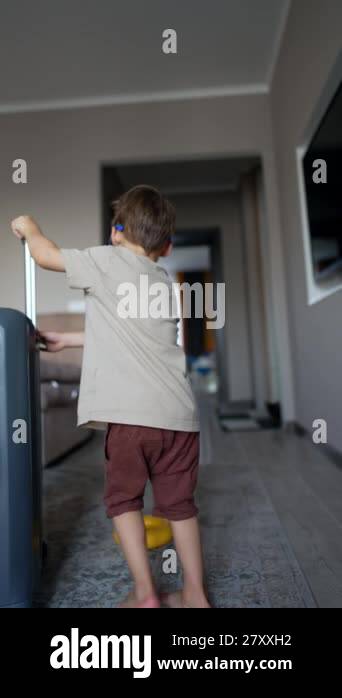 Rear view of a small kid wearing sunglasses and pushing a big grey ...