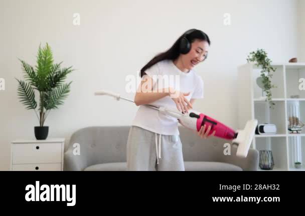 Asian young woman enjoying cleaning with headphones and vacuum. Happy ...