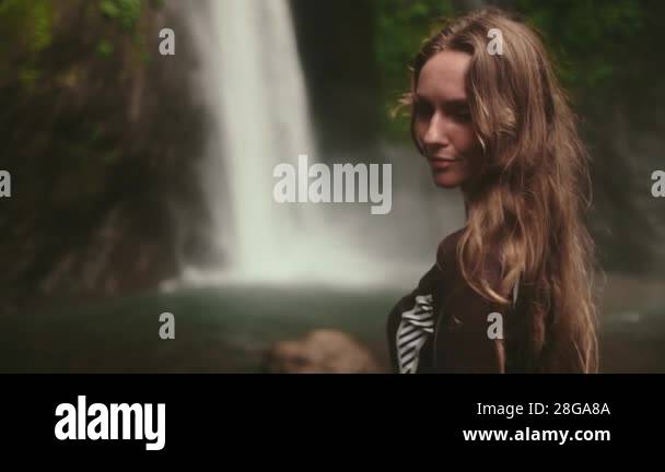 Woman standing in front of powerful Bali waterfall, surrounded by lush ...