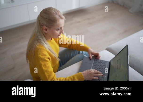 A young woman in a yellow sweater is seen using a laptop on a ...