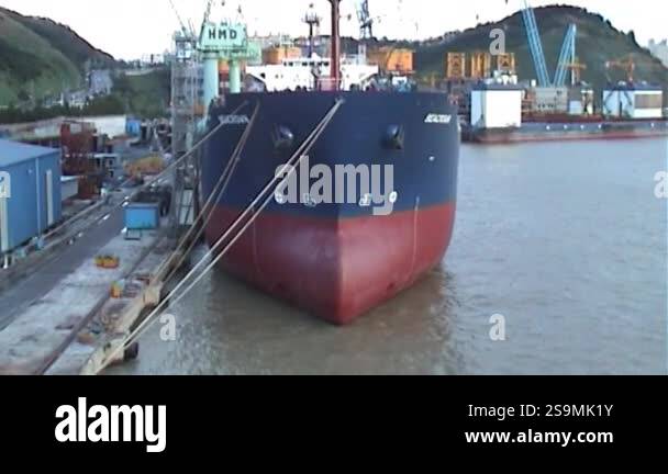 A large cargo ship, painted in a two-tone color scheme, is docked at a ...
