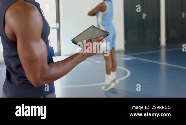 Coach holding tablet, observing basketball player practicing dribbling ...