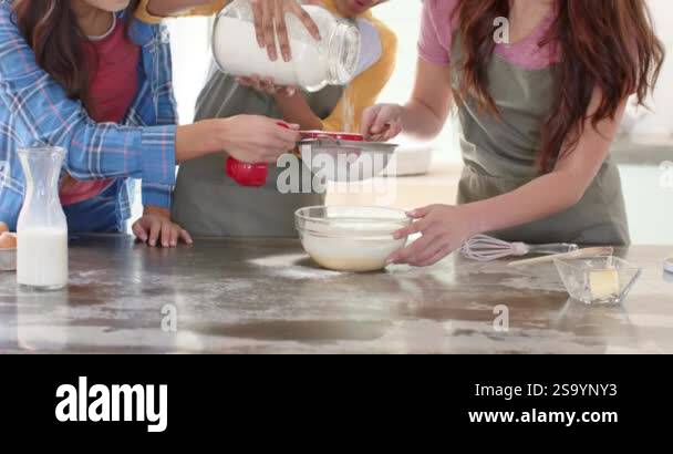 Women friends baking together in kitchen, sifting flour into mixing ...