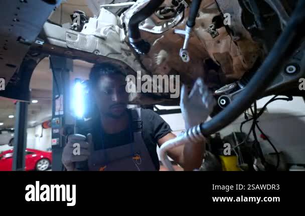 Auto mechanic inspecting the underside of a car engine with a ...