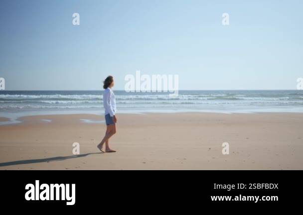 Woman strolling serene beach in summer sunlight. Carefree lady enjoying ...