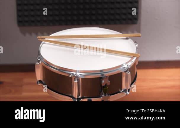 A detailed view of a snare drum with two wooden drumsticks resting on ...