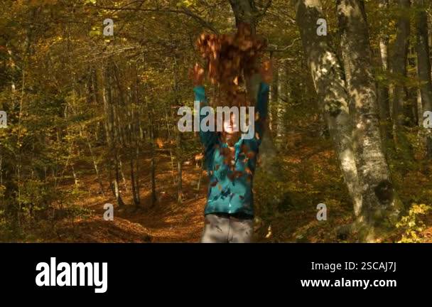 Woman joyfully tosses autumn leaves into air, her arms raised in ...