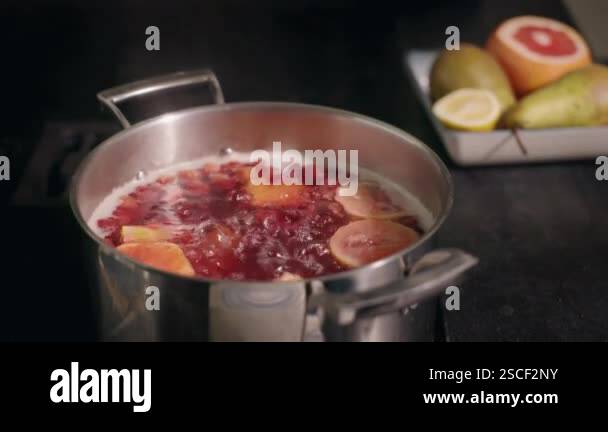 A pot of boiling fruit compote with vibrant citrus slices, with fresh ...