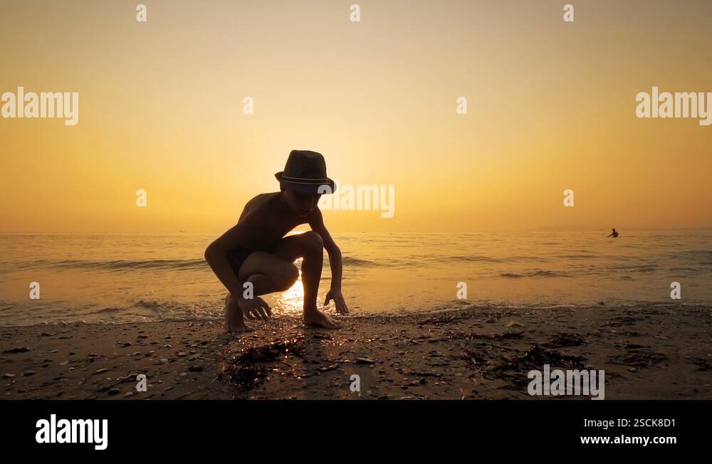 Little boy collects pebbles on the sea beach at sunset, SLOW MOTION