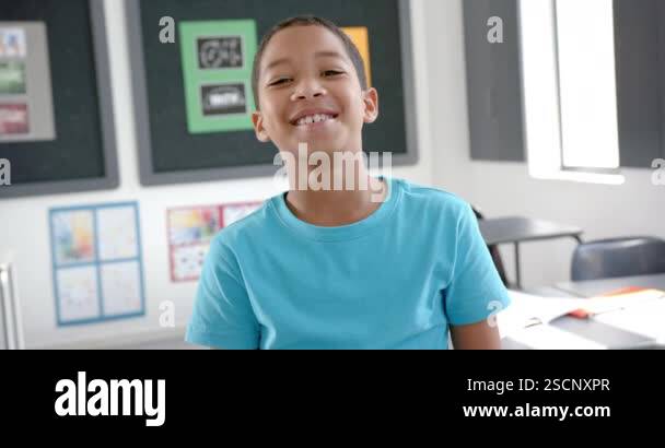 Biracial boy with a joyful smile, wearing a blue shirt, in a classroom ...