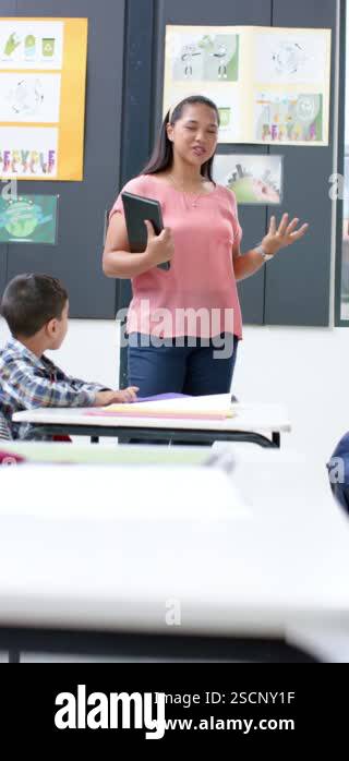 Vertical video: In school, middle-aged biracial female teacher holding ...