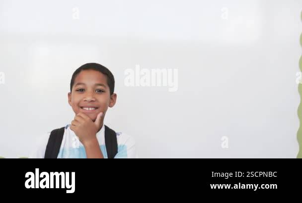 In school, young biracial male student wearing a backpack looks up ...