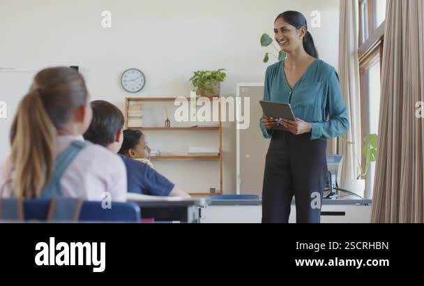 In school, teacher holding tablet and engaging with students in ...