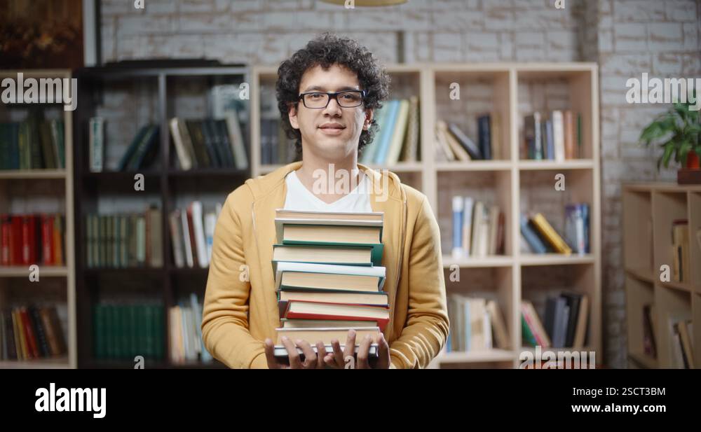 Asian guy with curly hair is standing between bookshelves of library ...