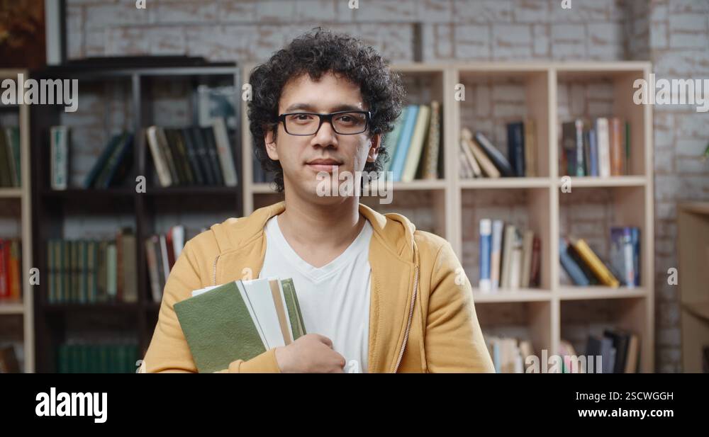 Asian guy with curly hair is standing between bookshelves of library ...