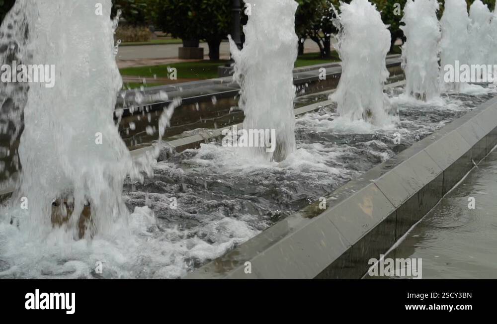 Foamy streams of water rise and fall. Alley of fountains in a city park ...