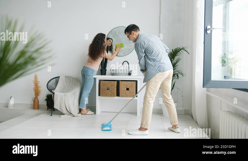 Young man and woman cleaning bathroom washing mirror mopping floor at ...