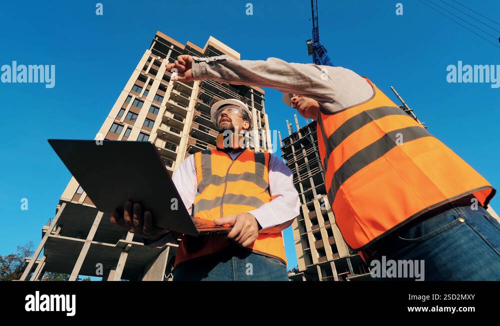 Male architects with a laptop and two high-rise buildings in progress ...