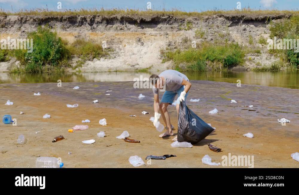 Angry man collects plastic trash on the banks of polluted river Stock ...