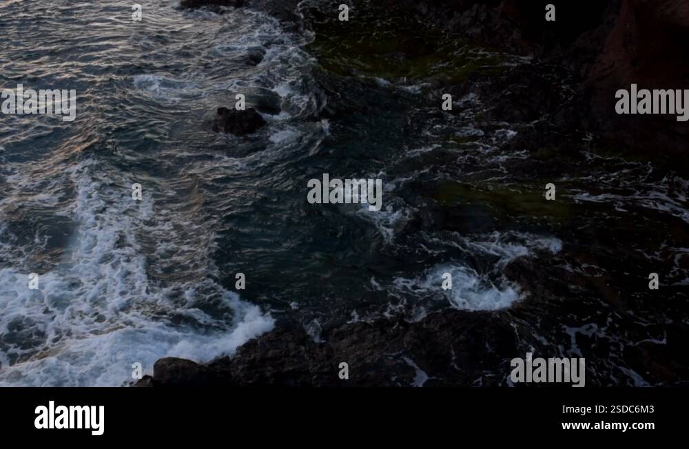 Ocean waves crash against the rocky shoreline as a traveler hikes up ...