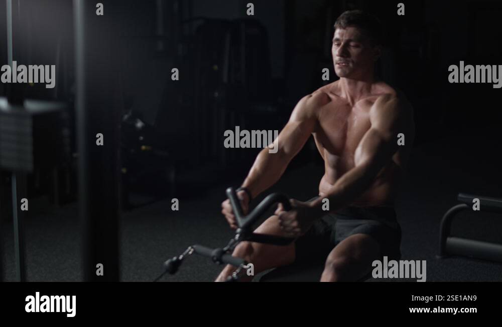 Athletic man in the Gym lifting blocks on rowing machine, training on ...