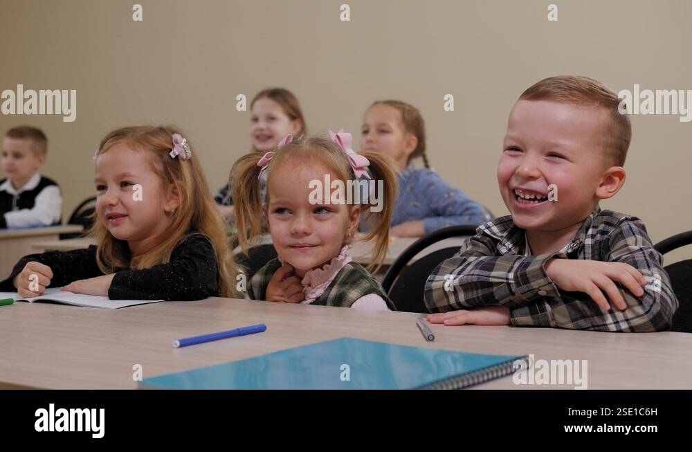 A group of children sit at a desk in an elementary school and laugh ...