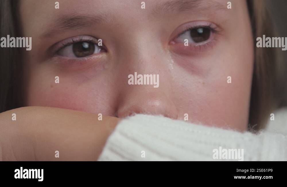 The girl is crying in the room sitting at the table and tears are ...