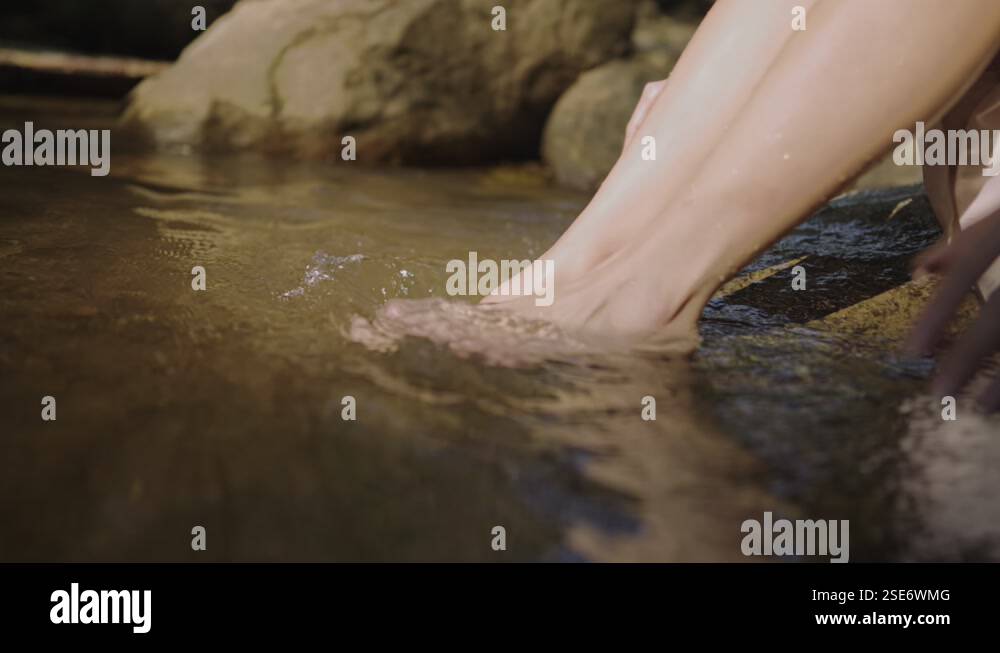 female soaking her feet in the canal river stream, hands playing with ...