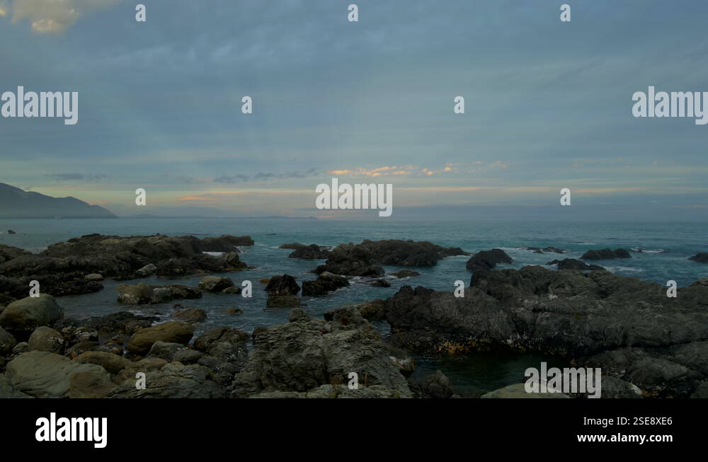 Sun rays on cloudy day above dark rocks at Kaikoura coast in New ...