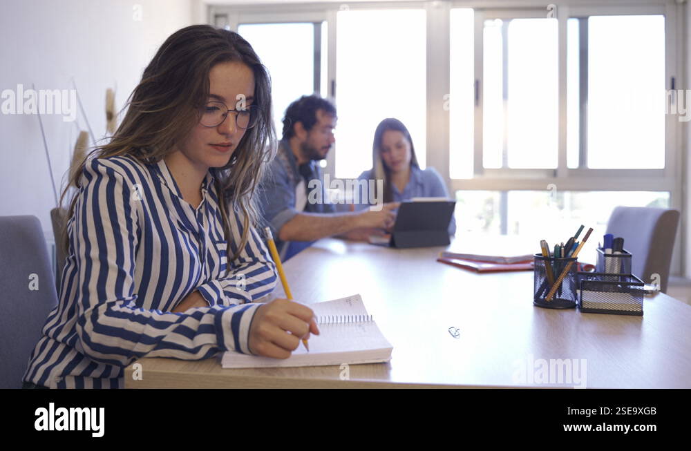 Side view of young woman taking notes and looking to camera while ...