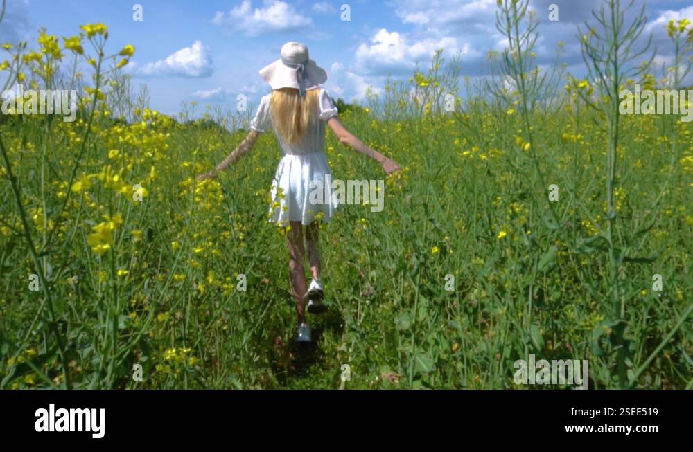 A young beautiful girl in a white dress in a wide hat walks through a ...