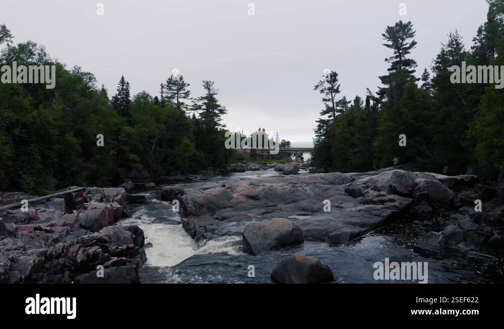 Flying low above the rocks down a river to a bridge in the distance on ...