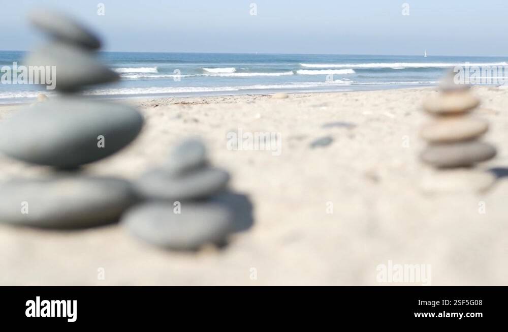 Rock balancing on ocean beach, stones stacking by sea water waves ...