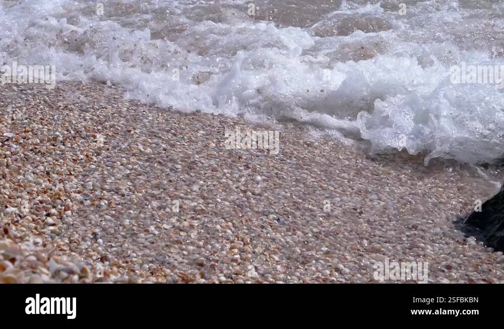 Sea Wave with Foams Rolls onto the Sandy Shore from Shells. Close up ...