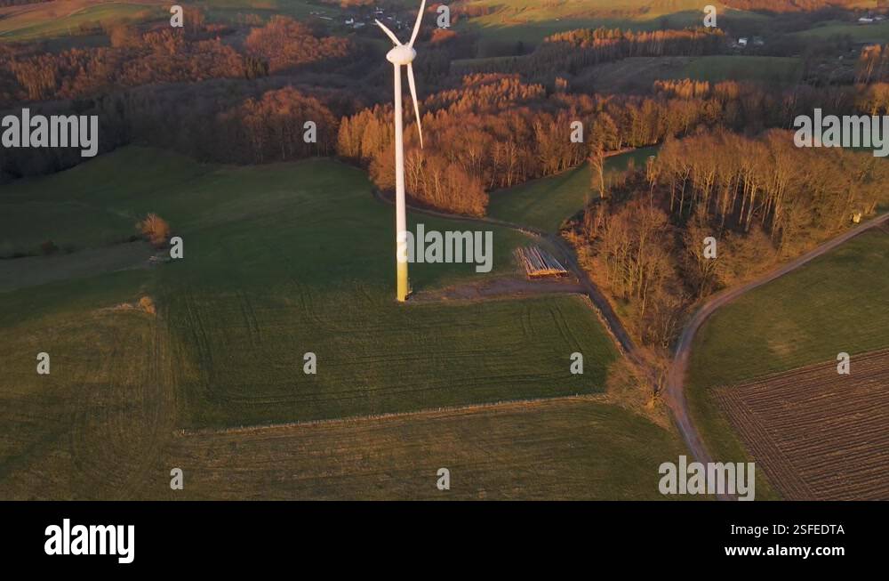A high windmill spinning fast in a lush, green field at sunset ...