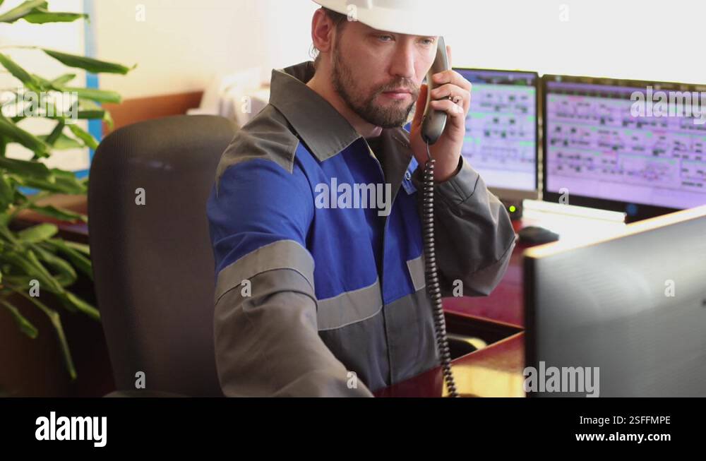 Operator in overalls answers a phone call while sitting in the control ...