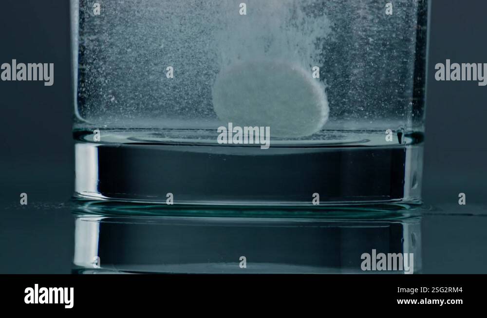 Dissolving Video Dropped medicine dissolving water glass closeup. White effervescent ...
