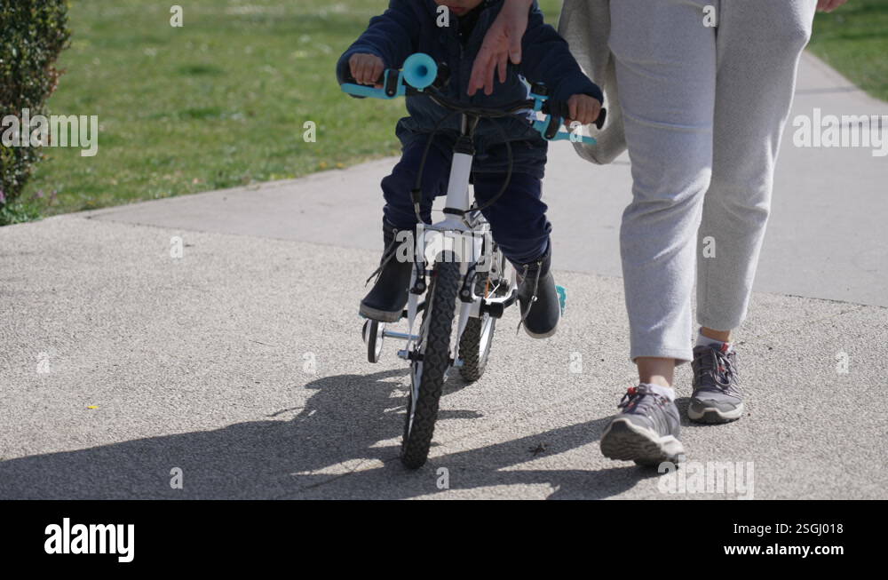 Little boy learning to ride bicycle with mother support. Mom helping ...