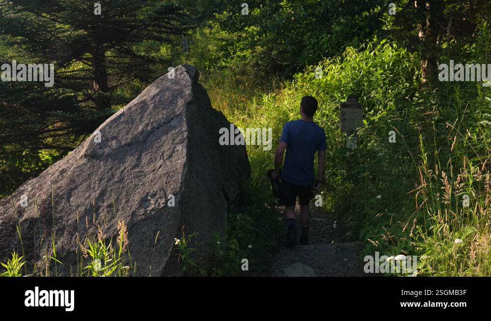 Hiker on a trail walks by a huge pointed granite rock in the forest ...