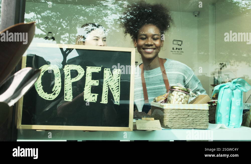 Two female shopkeepers place open sign board at store's glass windows ...