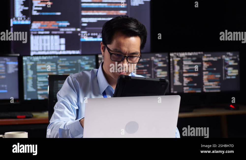 Asian Male Programmer Using Tablet While Writing Code By A Laptop Using ...