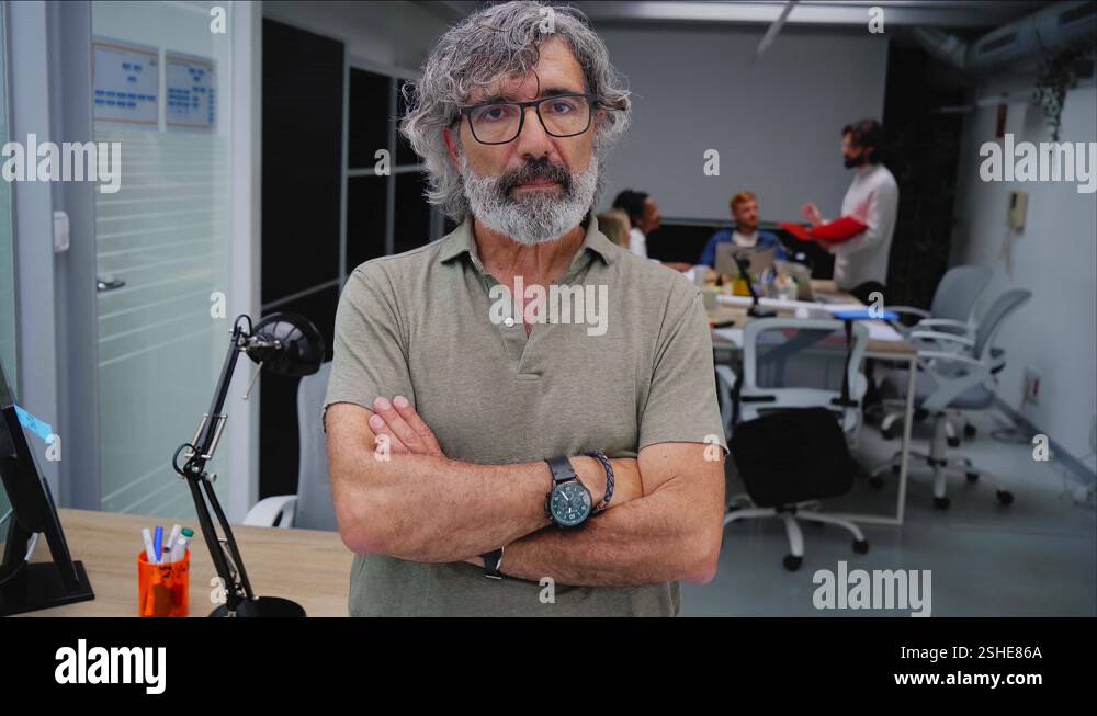 Serious mature businessman looking at camera standing in office at team ...