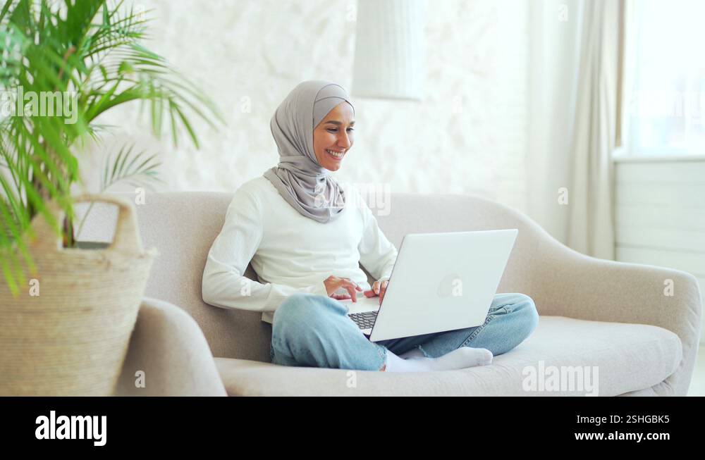 Smiling Muslim girl in hijab freelancer working on laptop checking ...
