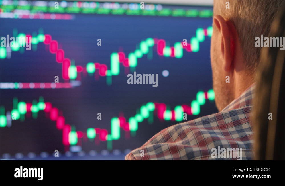 Trader works behind computer screens filled with charts and data ...