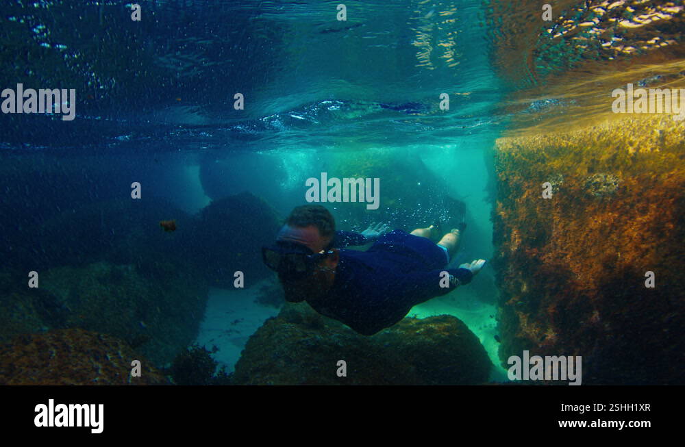 Man dives between rocks and swims underwater in the narrow channel ...