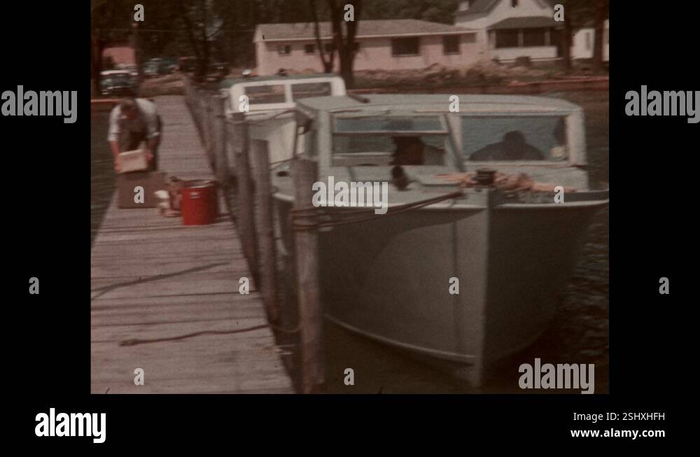 1960s: Man stands on dock, helps unload boat, holds box, armload of ...
