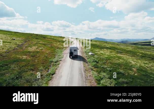 Drone follows 4x4 camper van drive on a gravel mountain road on sunny ...
